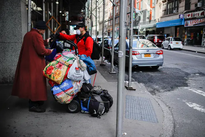 Felix Guzman, center, wears protective gloves and a mask due to COVID-19 concerns before handing out disposable gloves and sanitizing wipes to people who are homeless in midtown, in New York